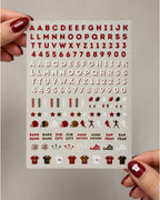 A sheet of nail stickers held by two hands with red nail polish. The sheet features the San Francisco 49ers colors (red, white, and brown) with various lettering, numbers, footballs, helmets, and team logos.