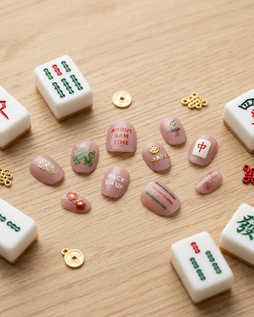 Press-on nails wearing mahjong stickers among tiles and gold charms: dragon, bam, flowers, and About Bam Time