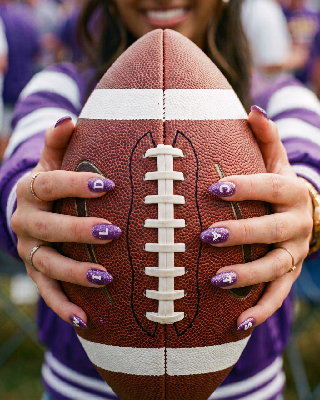 Fan in purple holding a football with purple and white game-day nail stickers