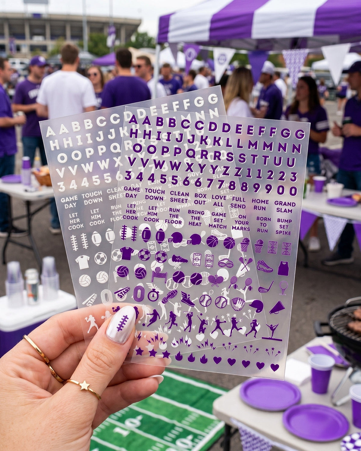 Hand holding the purple and white Northwestern nail sticker sheets at a tailgate, purple nails with letter stickers
