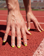 Runner in the starting position on a track wearing Volt Lime nails with white LFG letter stickers