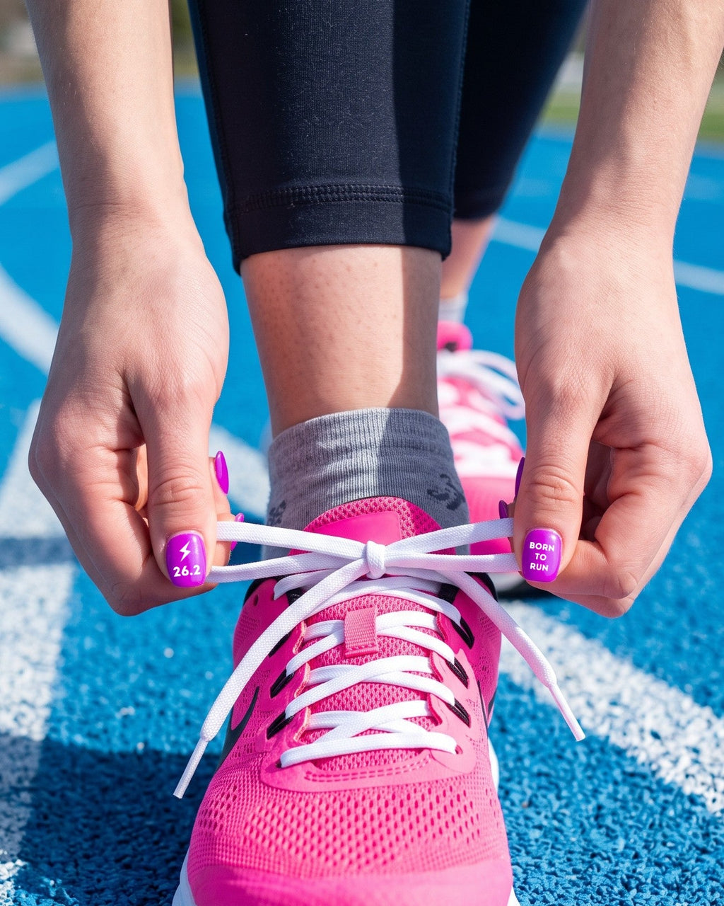 Tying a pink running shoe on the track with purple nails wearing 26.2 and Born to Run stickers