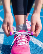 Tying a pink running shoe on the track with purple nails wearing 26.2 and Born to Run stickers